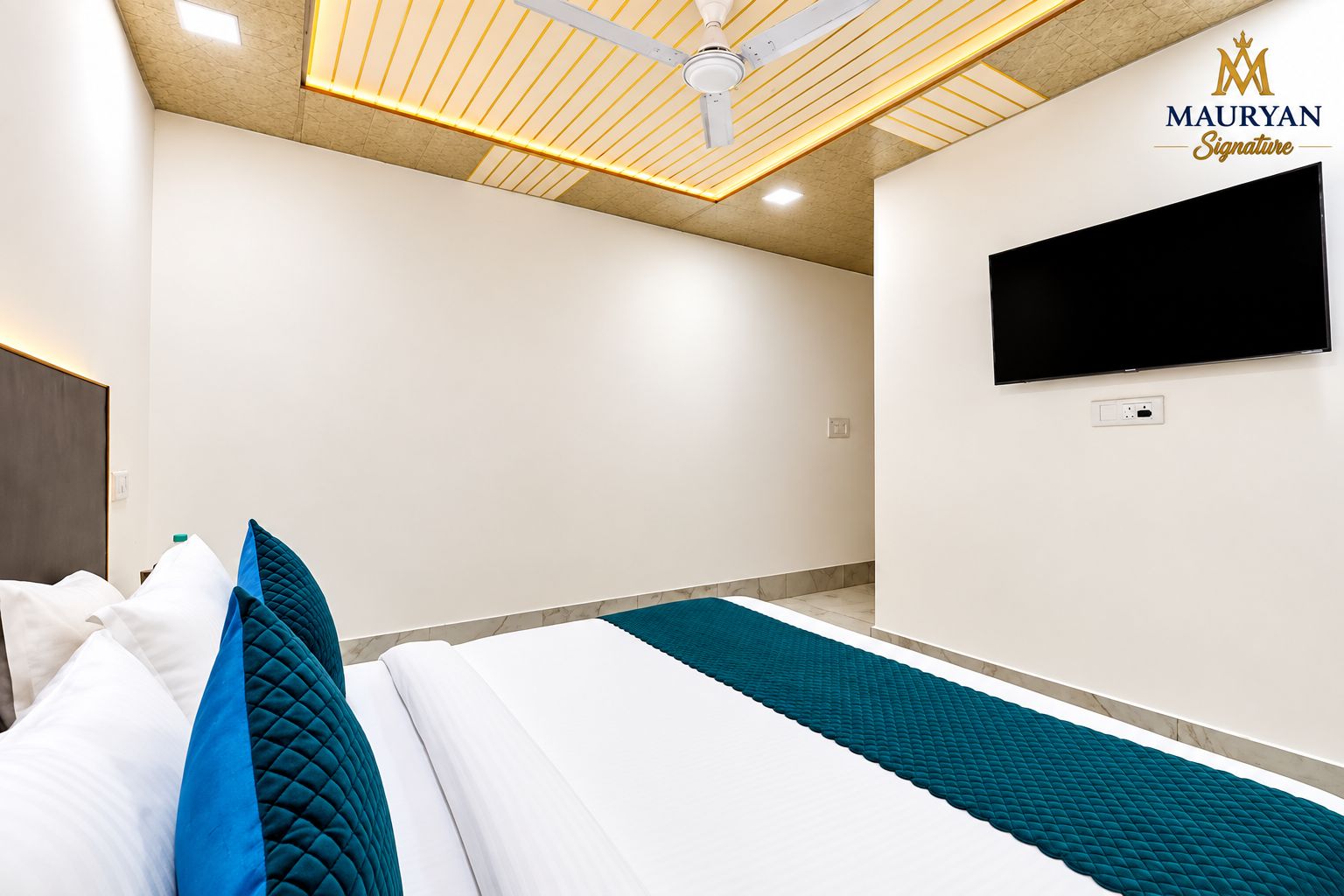 A hotel room with a bed, a flat-screen TV mounted on the wall, a ceiling fan, and a marble floor.
