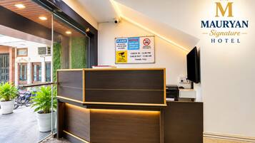 A hotel reception desk with a sign indicating check-in and check-out times, surveillance notice, and smoking prohibition.