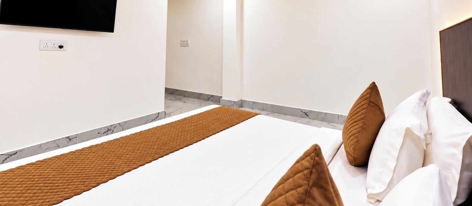 Une chambre d’hôtel avec un lit, un téléviseur à écran plat fixé au mur et un sol à motifs de marbre.