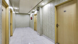 A hallway with marble tiled floors, wooden doors, and a fire extinguisher on the wall. - Mauryan Signature hotel Devli Khanpur (New Delhi)