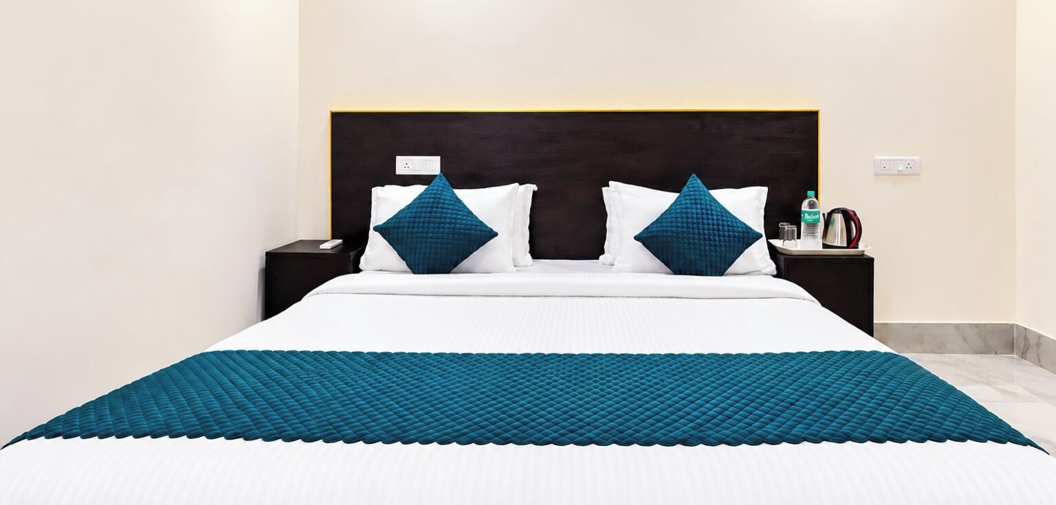 A hotel room with a large bed, two bedside tables, a nightstand, and a wall socket.