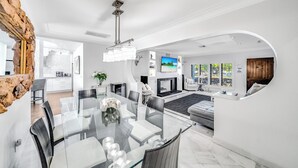 Una sala de estar moderna con una mesa de comedor de vidrio, asientos cómodos, una chimenea y una televisión.