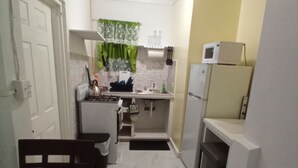 Cocina compacta con refrigerador, microondas, lavaplatos y estufa. Hay una mesa de comedor con sillas y un pequeño basurero.