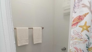 Un área de ducha con suelo de baldosas, una cortina de baño con motivos marinos y dos toallas blancas colgadas en un perchero.