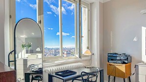 Un espacio de oficina moderno con un ventanal que ofrece vistas de la ciudad, un escritorio con computadora e impresora, y un radiador debajo de la ventana.