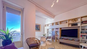 Una sala de estar moderna con un televisor grande, estanterías, un comedor y vistas a la ciudad.