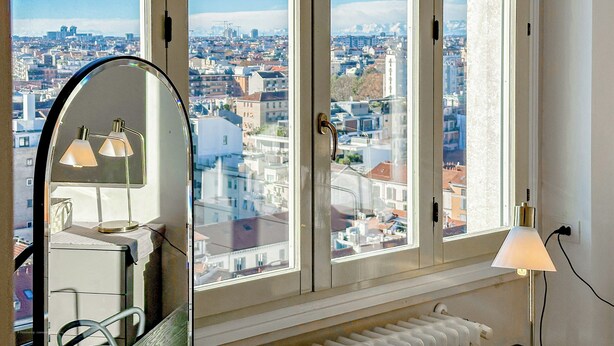 Una habitación con un ventanal grande que ofrece vistas a la ciudad, un escritorio con una lámpara y un radiador.
