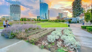 A cityscape with modern buildings, a large open park area with grass and plants, and a clear sky.