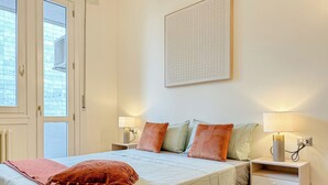 A bedroom with a bed, two bedside tables, a nightstand, a window, and a wall-mounted artwork.