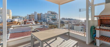Une terrasse sur le toit, avec une table et des bancs, offrant une vue sur un paysage urbain composé d’immeubles et d’un ciel dégagé.