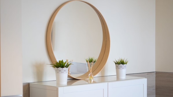 Un mueble blanco con tres plantas en macetas y un espejo grande.