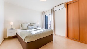 A bedroom with a bed, bedside table, lamp, and an air conditioning unit.