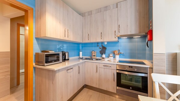 A modern kitchen with wooden cabinets, a microwave, a kettle, and a stove.