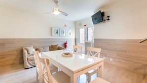 A modern kitchen with a dining area, wooden flooring, a ceiling fan, and a mounted flat-screen TV.