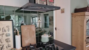 Une cuisine équipée d’une cuisinière à gaz, d’une planche à découper en bois, d’une estampe botanique encadrée et d’un meuble de rangement.
