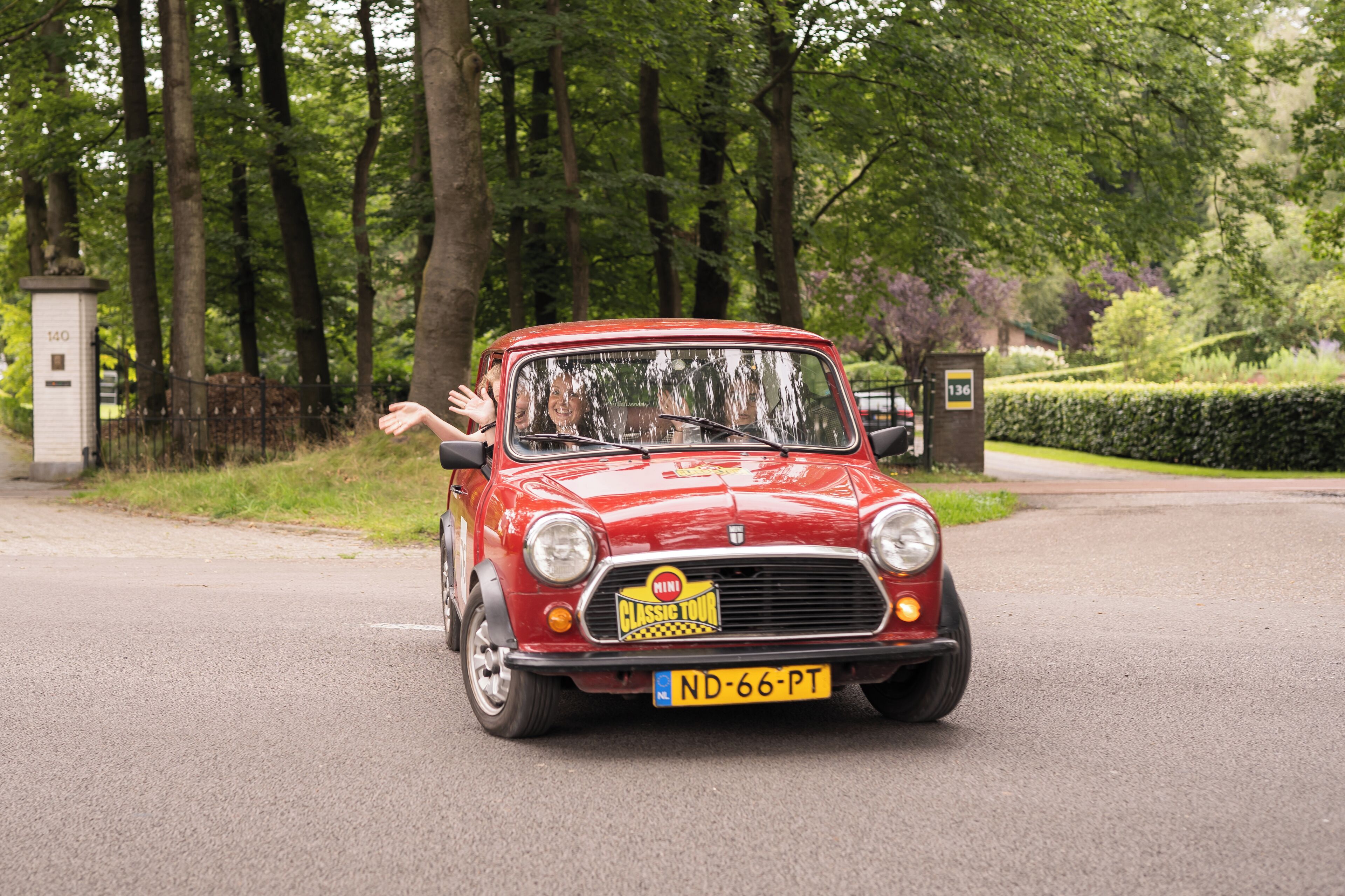A red classic car with a visible license plate on a paved road.