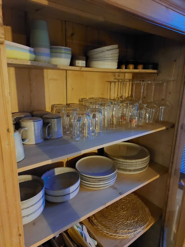 A wooden shelf unit with various kitchenware including plates, bowls, and glassware.