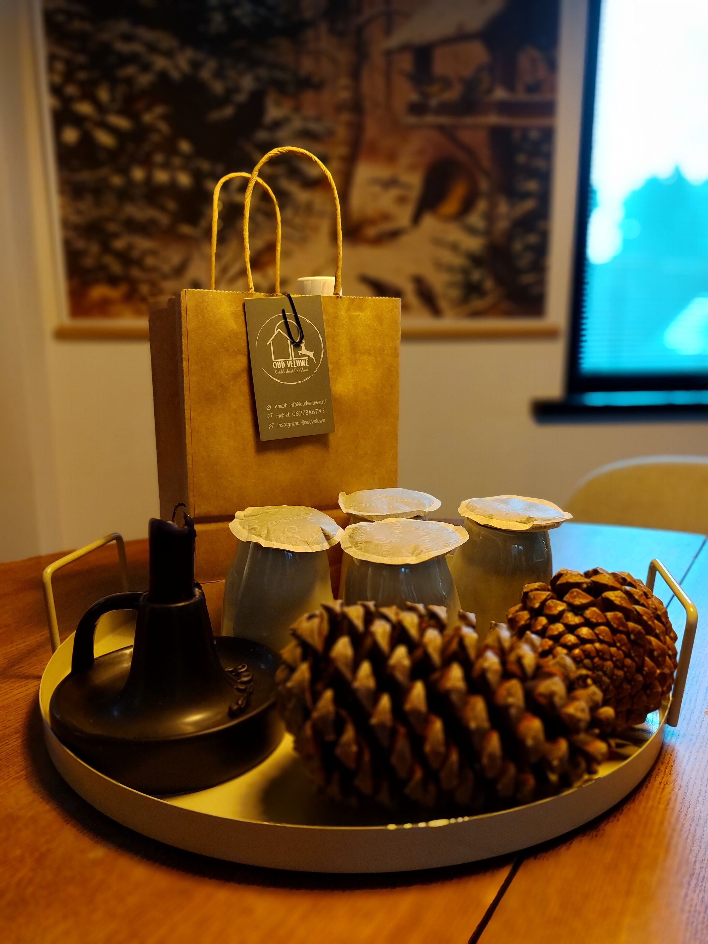 Un vassoio con una pigna, candele e un sacchetto regalo su un tavolo di legno.