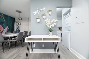 Una cocina moderna con armarios blancos, horno empotrado y zona de comedor con mesa y sillas blancas.