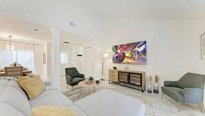 Ein modernes Wohnzimmer mit einer Couch, Sesseln, einem Couchtisch und einem an der Wand befestigten Fernseher.