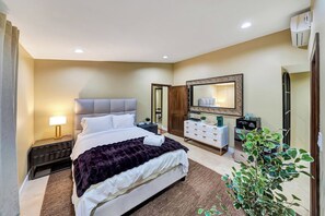 A hotel room with a bed, bedside table, lamp, dresser, mirror, and a potted plant.