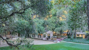 A courtyard with a small building, a wooden deck, and surrounding greenery.