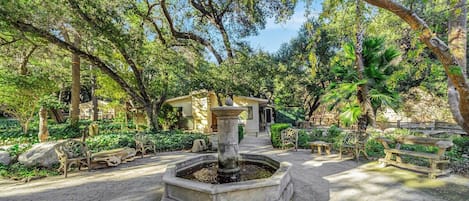 A courtyard with a central fountain, surrounded by benches and trees.