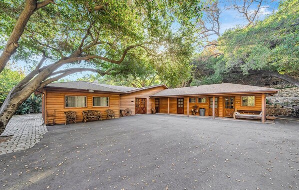 A wooden cabin with a covered porch, a stone wall, and a paved driveway.