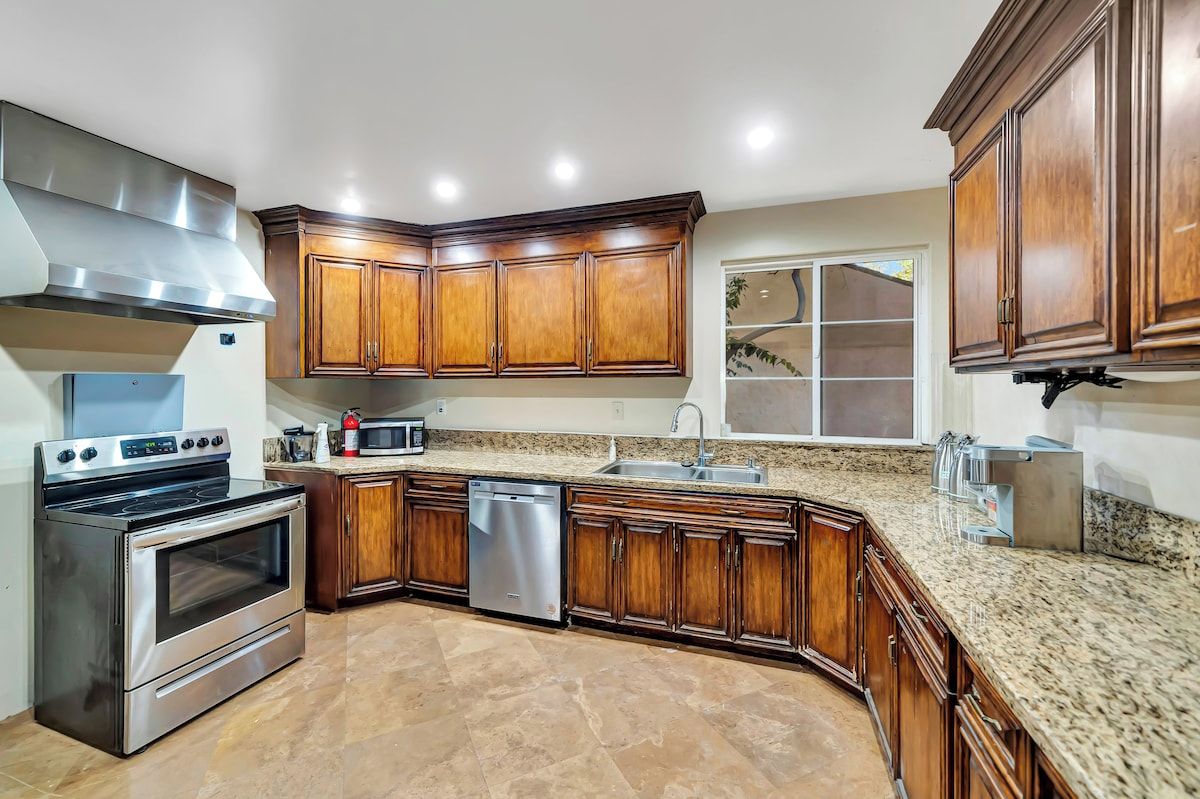 Una cocina con armarios de madera, electrodomésticos de acero inoxidable, encimeras de granito y una ventana con vistas.