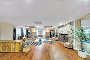 A spacious living area with a stone fireplace, wooden flooring, and a large window.