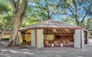 A covered outdoor seating area with chairs and tables, surrounded by trees.