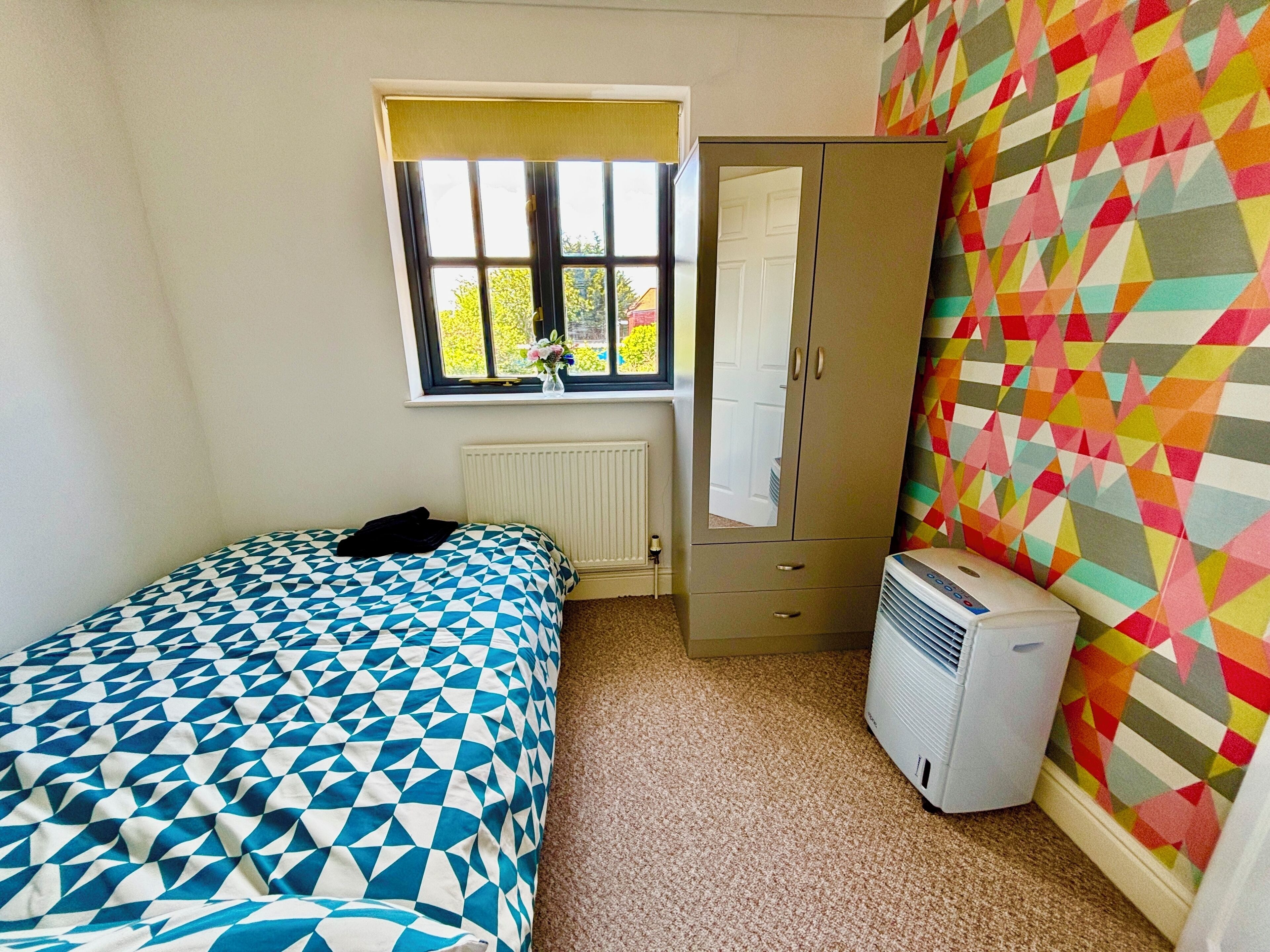 A bedroom with a bed, wardrobe, radiator, window, and air conditioner.
