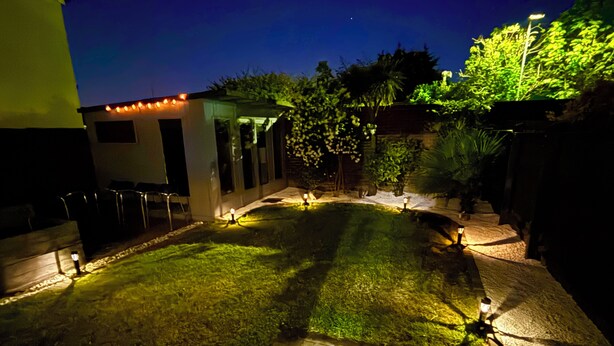 A nighttime outdoor patio area with a paved walkway, seating, and ambient lighting.