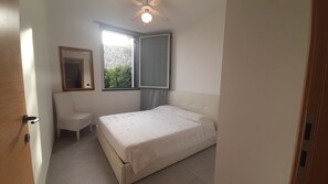 A bedroom with a bed, a chair, a window with curtains, and a ceiling fan.