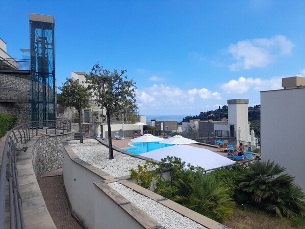 A rooftop pool area with a clear view of the sea, surrounded by buildings and a stone staircase.