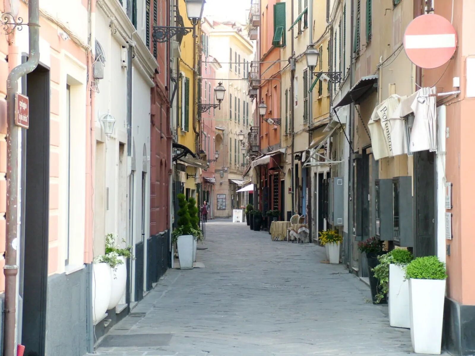 A narrow street lined with colorful buildings, a no entry sign, and outdoor seating areas.