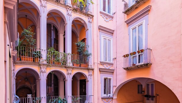 A courtyard with a cobblestone floor, multiple arches, and balconies with plants. - Palazzo Loffredo by NapoliApartments (Naples)