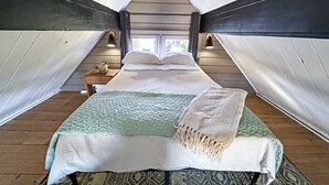 A cozy attic bedroom with a bed, pillows, a nightstand, and a lamp. - Cozy 2-bedroom A-Frame near the Lake (Manhattan)