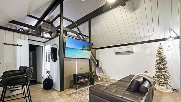 A modern living room with a fireplace, a large TV, a Christmas tree, and a leather sofa. - Cozy 2-bedroom A-Frame near the Lake (Manhattan)
