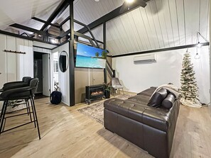 A modern living room with a fireplace, a large TV, a Christmas tree, and a leather sofa.