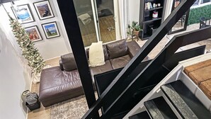 A modern living room with a brown leather sofa, a small coffee table, and a staircase leading to an upper level. - Cozy 2-bedroom A-Frame near the Lake (Manhattan)