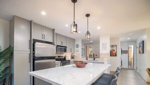 Cocina moderna con una isla grande, electrodomésticos de acero inoxidable e iluminación colgante.