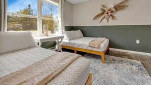 Un dormitorio con dos camas, una ventana con vistas a árboles y un adorno en la pared.