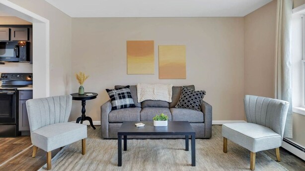 Una sala de estar moderna con un sofá gris, dos sillones, una mesa de centro y obras de arte en la pared.