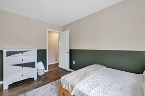 A bedroom with a bed, a dresser, and a door leading to another room.
