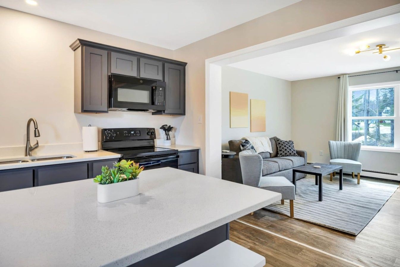 A modern kitchen with dark cabinets, a stainless steel microwave, and a large island with a plant.