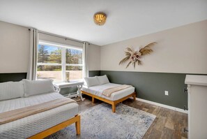 A bedroom with two beds, a window with a view, a wall-mounted decorative piece, and a ceiling light fixture.