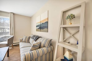 A living room with a striped sofa, a chair, a bookshelf, and a painting on the wall.