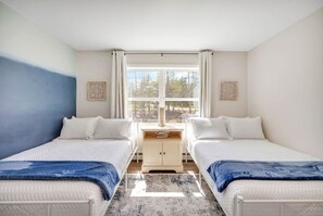 A bedroom with two beds, a desk, and a window.
