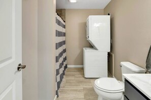 Un bagno funzionale con il water, una lavatrice e una tenda per la doccia.